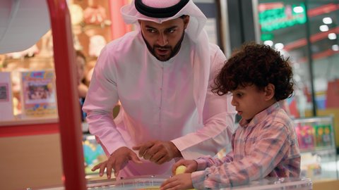 أجواء مليئة بالمرح والحماس، تصوير لرجل عربي خليجي إماراتي يرتدي الكندورة والغترة يشارك ابنه لحظات ممتعة في لعبة الهوكي الهوائي فى أحد المراكز الترفيهية في الإمارات، الأنشطة الرياضية الممتعة