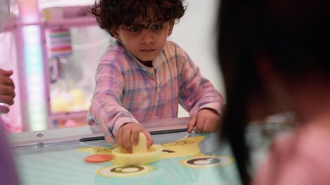 منافسة مليئة بالتحدي والإثارة ، أجواء مليئة بالمرح والحماس ،تصوير مقرب لطفل عربي خليجي إماراتي يرتدي الزى الكاجوال ، يستمتع بلعبة الهوكي الهوائي برفقة اخته ، التفاعل بين أفراد العائلة، الأنشطة الرياضية الممتعة