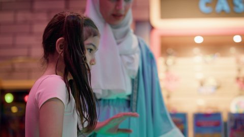 ايماءات المرح والحماس، مراكز الالعاب الترفيهيه في الامارات، قضاء اوقات ممتعه ، تصوير لطفلة عربية خليجية إماراتية ترتدي الزى الكاجوال ، تستمتع بلعب الهوكي الهوائي برفقة والدتها ، طاولة مضيئة بألوان زاهية