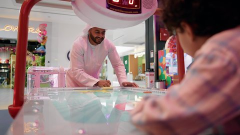قضاء الاوقات الممتعه مع الابناء ، ايماءات التحدى والحماس ، تصوير لرجل عربي خليجي اماراتي يرتدي الكندورة والغترة ، يلعب الهوكي الهوائي مع ابنه ، طاولة مضيئة بألوان زاهية ، مراكز الالعاب الترفيهيه في الامارات