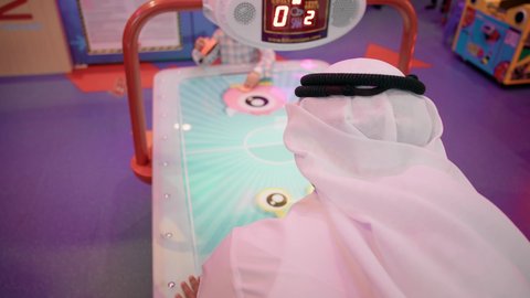 طاولة مضيئة بألوان زاهية ، أجواء عائلية ممتعة ، تصوير لرجل عربي خليجي اماراتي يرتدي الكندورة والغترة ، يلعب الهوكي الهوائي مع ابنه ، مراكز الالعاب الترفيهيه في الامارات  ، تعابير التحدي والحماس