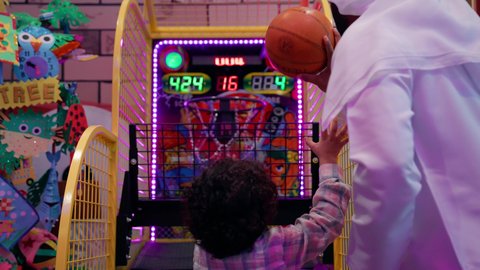 دمج التقنيات الحديثه فى ألعاب الاطفال، قضاء اوقات ممتعه مع العائله، مراكز الالعاب الترفيهيه في الامارات، تصوير من الخلف لرجل عربي خليجي غماراتي يرتدي الغترة والكندورة يقوم يمشاركة ابنه لعبة رمي كرة السلة، قضاء وقت ممتع باللعب والتركيز، تعزيز المهارات الذهنية