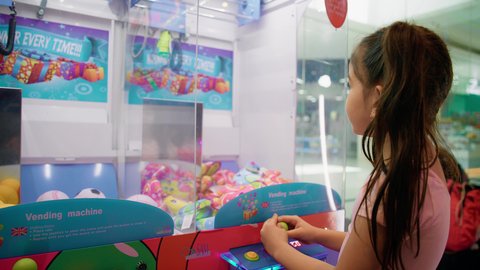 التركيز والقدرة على التحكم، الشعور بالمتعة والفرح، بنت سعودية تقضي وقت ممتع في المراكز الترفيهية في الامارات، صالات ألعاب الأركيد المتطورة، تصوير من الجانب لفتاة عربية خليجية اماراتية ترتدي الزي الكاجوال تلعب آلة مخلب الالتقاط الالكترونية، قسم التحديات والمغامرات.