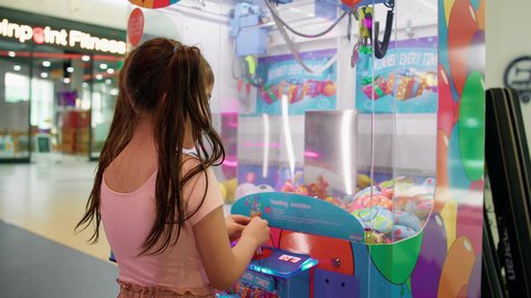 قسم التحديات والمغامرات، التركيز والقدرة على التحكم، الشعور بالمتعة والفرح، بنت سعودية تقضي وقت ممتع في المراكز الترفيهية في الامارات، صالات ألعاب الأركيد المتطورة، تصوير من الخلف لفتاة عربية خليجية اماراتية ترتدي الزي الكاجوال تلعب آلة مخلب الالتقاط الالكترونية.