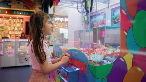 الشعور بالمتعة والفرح، بنت سعودية تقضي وقت ممتع في المراكز الترفيهية في الامارات، التركيز والقدرة على التحكم، صالات ألعاب الأركيد المتطورة، تصوير من الجانب لفتاة عربية خليجية اماراتية ترتدي الزي الكاجوال تلعب آلة مخلب الالتقاط الالكترونية، قسم التحديات والمغامرات.