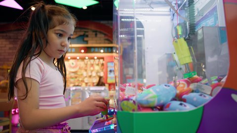 التركيز والقدرة على التحكم، الشعور بالمتعة والفرح، بنت سعودية تقضي وقت ممتع في المراكز الترفيهية في الامارات، صالات ألعاب الأركيد المتطورة، تصوير من الجانب لفتاة عربية خليجية اماراتية ترتدي الزي الكاجوال تلعب آلة مخلب الالتقاط الالكترونية، قسم التحديات والمغامرات.