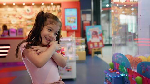 الانتصار والفوز بلعبة آلة مخلب الالتقاط الالكترونية، صالات ألعاب الأركيد المتطورة، قسم التحديات والمغامرات، بنت سعودية تقضي وقت ممتع في المراكز الترفيهية في الامارات، تصوير مقرب لفتاة عربية خليجية اماراتية ترتدي الزي الكاجوال تمسك لعبتها بتعابير السرور والسعادة