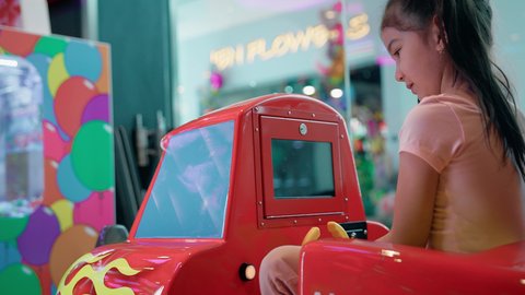 صالات الألعاب المتطورة، أجواء تفاعلية مبهجة، المتعة والتسلية في المراكز الترفيهية في الامارات، الشعور بالحماس والفرح، فتاة عربية خليجية اماراتية ترتدي الزي الكاجوال تمسك مقود سيارة الأطفال الكهربائية، التركيز والقدرة على التحكم .