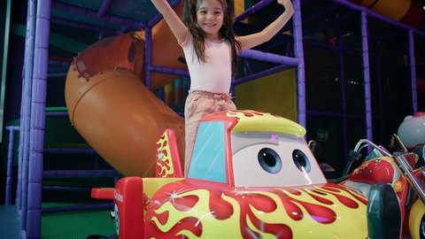 ايماءات السعادة والسرور، المتعة والتسلية في المراكز الترفيهية في الامارات، الشعور بالحماس والفرح، صالات الألعاب المتطورة، أجواء تفاعلية مبهجة، فتاة عربية خليجية اماراتية ترتدي الزي الكاجوال تقف في لعبة سيارة الأطفال الكهربائية