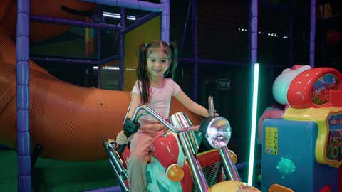 الاستمتاع بقضاء الاجازة الصيفيه في احدى الصالات في الأماكن الترفيهية في الامارات، النظر إلى الكاميرا بايماءات السعادة والمتعة، العاب الاركيد الالكترونيه المتطورة، فتاة عربية خليجية اماراتية ترتدي الزي الكاجوال وتقوم بركوب الدباب الكهربائي