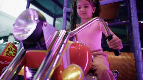 العاب الاركيد الالكترونيه المتطورة، الاستمتاع بقضاء الاجازة الصيفيه في احدى الصالات في الأماكن الترفيهية في الامارات،ايماءات الاندماج و التركيز، فتاة عربية خليجية اماراتية ترتدي الزي الكاجوال وتقوم بركوب الدباب الكهربائي