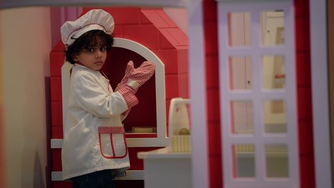 النظر إلى الكاميرا بايماءات الثقة بالنفس، وظائف ومهن مستقبلية، دعم وتنمية مهارات الطبخ عند الأطفال، الاستمتاع في اللعب في مركز الالعاب الترفيهيه، ولد عربي خليجي إماراتي يرتدي زي الشيف الخاص يضع في يده قفازات الطبخ