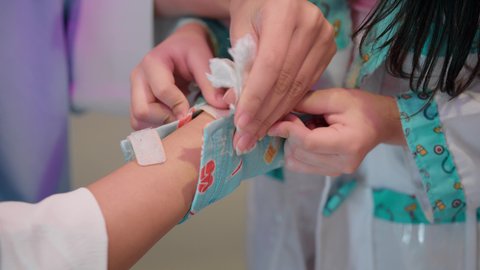 الاستمتاع في مركز الالعاب الترفيهي، مفهوم التعليم عن طريق اللعب، تعريف الأطفال على المهن المستقبلية، أم إماراتية ترتدي عباءة تقوم باللعب مع ابنتها، الطب والرعاية الصحية، تصوير مقرب لفتاة عربية خليجية سعودية ترتدي الزي الطبي تقوم بمعالجة يد والدتها