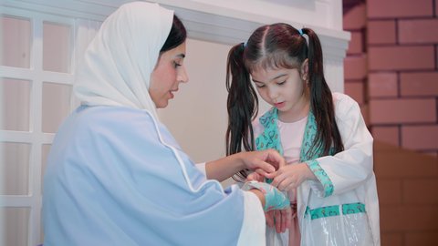 تعريف الأطفال على المهن والوظائف المستقبلية، أم إماراتية محجبة ترتددي عباءة تقوم باللعب مع ابنتها، الطب والرعاية الصحية، فتاة عربية خليجية سعودية ترتدي الزي الطبي تقوم بمعالجة يد والدتها، مفهوم التعليم عن طريق اللعب، الاستمتاع في مركز الالعاب الترفيهي