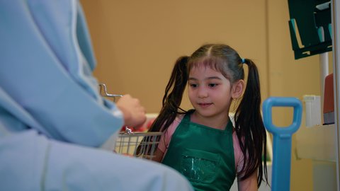 مفهوم الغذاء الصحي، تنمية ودعم مهارات الأطفال، تعليم الابناء تسوق الخضار الطازجة، قضاء وقت ممتع في مركز الالعاب الترفيهيه، فتاة عربية خليجية سعودية ترتدي مئرز الطبخ، تصوير مقرب لسيدة عربية خليجية إماراتية تقوم بمشاركة ابنتها لحظات المرح