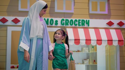 تعليم الابناء تسوق المنتجات الطازجة من قسم البقالة، قضاء وقت ممتع في مركز الالعاب الترفيهيه، فتاة عربية خليجية سعودية ترتدي مئرز الطبخ، دعم وتنمية مهارات الأطفال، سيدة عربية خليجية إماراتية محجبة تقوم بمشاركة ابنتها لحظات المرح، تعابير السرور والسعادة