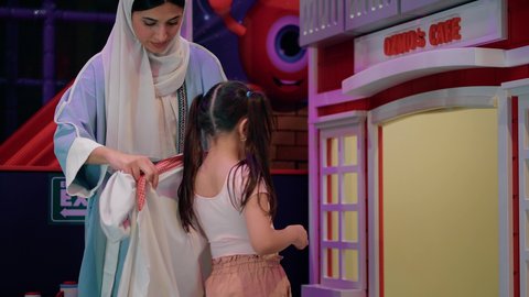 قضاء وقت ممتع في مركز الالعاب الترفيهيه، وظائف ومهن مستقبلية، تنمية مهارات الطبخ عند الأطفال، الاستعداد لدخول ركن الطبخ والطهي، فتاة عربية خليجية سعودية ترتدي زي الطهاة، أم عربية خليجية إماراتية ترتدي العباءة تقوم بمساعدة بنتها بارتداء زي الشيف الخاص