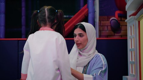 وظائف ومهن مستقبلية، تنمية مهارات الطبخ عند الأطفال، الاستعداد لدخول ركن الطبخ والطهي، قضاء وقت ممتع في مركز الالعاب الترفيهيه، فتاة عربية خليجية سعودية ترتدي زي الطهاة، تصوير مقرب لسيدة عربية خليجية إماراتية تقوم بمساعدة بنتها بارتداء زي الشيف الخاص