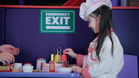 Enjoy playing at the entertainment games center, developing cooking skills in children, expressions of happiness and pleasure, an Arab -Gulf Arab girl who wears a special chef costume stands in front of a table with a set of cooking tools, future professions and functions, girls' passion for kitchen and cooking