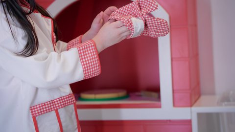 Future jobs and professions, support and development of children's cooking skills, girls' passion for kitchen and cooking, enjoying playing at the entertainment games center, closer photography of an Arab Gulf -Emirati girl who wears a special chef costume in her hand cooking gloves in her hand