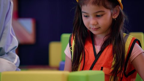Spending fun times playing and concentrating, entertainment centers in the Emirates, enhancing mental and intellectual skills, a close-up of an Emirati Gulf Arab girl wearing a helmet and a protective vest, a Saudi Gulf Arab mother assembling blocks with her daughter, nurturing and developing children's skills