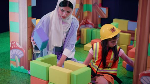 مراكز الالعاب الترفيهيه في الامارات، تعزيز المهارات الذهنية والفكرية، الاهتمام بالأبناء ودعمهم، قضاء أوقات ممتعة باللعب والتركيز، طفلة عربية خليجية إماراتية ترتدي الزى الكاجوال، ام عربية خليجية سعودية تقوم بتركيب المكعبات مع ابنتها، رعاية وتطوير مهارات الأطفال