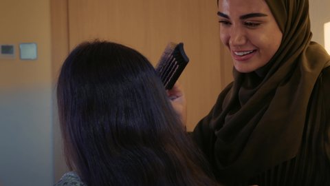 ايماءات السعادة و السرور ، حنان الأمهات و تحمل المسؤولية والعناية بالابناء، المحافظة على شعر صحي وأنيق، الاعتناء بالمظهر الخارجي، تصوير مقرب لأم عربية خليجية اماراتية ترتدي عباءه ملونه  تجلس على السرير تقوم بتصفيف شعر ابنتها و تقبلها