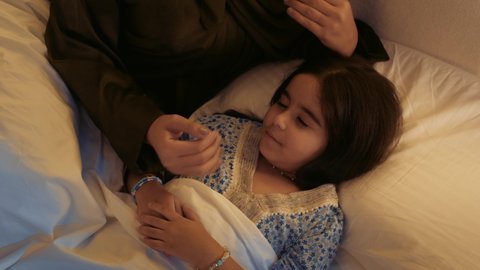 الشعور بالأمان في حضن الامهات، سيدة سعودية تقبل طفلتها في السرير بإيماءات الاهتمام والحب، أم عربية خليجية اماراتية تحضن صغيرتها بعطف وعناية، مفهوم عاطفة الأمومة وأهميتها للطفل، تعزيز وتمكين الروابط الأسرية