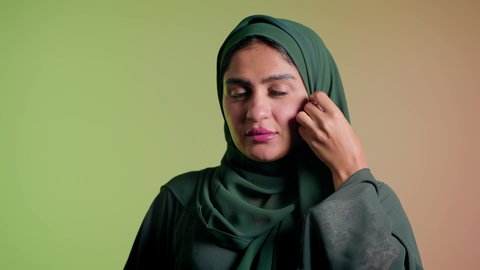 الإهتمام بالموضة والجمال والأناقة، تصوير مقرب لإمرأة عربية سعودية خليجية تنظر إلى الكاميرا بإيماءات الثقة بالنفس، عرض الملابس والاكسسوارات النسائية السعودية، ترتيب الحجاب والاستعداد للذهاب، ارتداء عباءة ملونة عصرية، خلفية ملونة