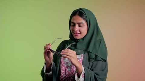 اتباع آخر صيحات الموضة, تصوير مقرب لإمرأة عربية خليجية سعودية مبتسمة ترتدي الحجاب والعباءة تقوم بوضع النظارة، الأناقة والاهتمام بالمظهر الخارجي، سيدة اماراتية تقوم بالعروض الإعلانية التسويقية للمنتجات المحلية، عرض احدث موديلات النظارات الشمسية، خلفية ملونة