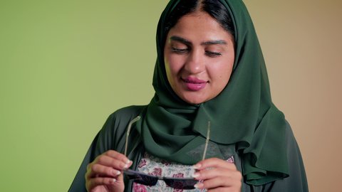 متابعة آخر صيحات الموضة, تصوير مقرب لإمرأة عربية خليجية سعودية مبتسمة ترتدي الحجاب والعباءة تقوم بوضع النظارة، الأناقة والاهتمام بالمظهر الخارجي، سيدة اماراتية تقوم بالعروض الإعلانية التسويقية للمنتجات المحلية، عرض احدث موديلات النظارات الشمسية، خلفية ملونة