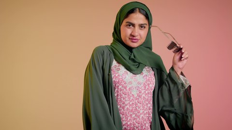 متابعة آخر صيحات الموضة, تصوير مقرب لإمرأة عربية خليجية سعودية مبتسمة ترتدي الحجاب والعباءة تقوم بوضع النظارة، الأناقة والاهتمام بالمظهر الخارجي، سيدة اماراتية تقوم بالعروض الإعلانية التسويقية للمنتجات المحلية، عرض احدث موديلات النظارات الشمسية، خلفية ملونة