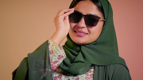 متابعة آخر صيحات الموضة, تصوير مقرب لإمرأة عربية خليجية سعودية مبتسمة ترتدي الحجاب والعباءة تقوم بوضع النظارة، الأناقة والاهتمام بالمظهر الخارجي، سيدة اماراتية تقوم بالعروض الإعلانية التسويقية للمنتجات المحلية، عرض احدث موديلات النظارات الشمسية، خلفية ملونة
