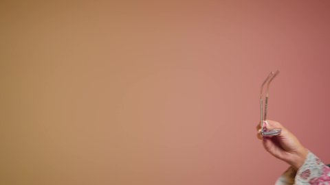 ايماءات الانوثة والسرور، ارتداء النظارة والاهتمام بالمظهر الخارجي والاناقة الشخصية، سيدة اماراتية تقوم بعرض احدث موديلات النظارات الشمسية، تصوير مقرب لإمرأة عربية خليجية سعودية مبتسمة ترتدي الحجاب والعباءة تقوم بالتسويق للمنتجات المحلية، خلفية ملونة