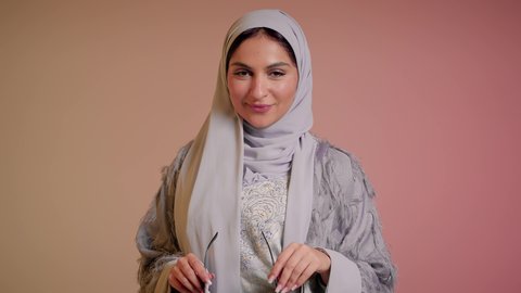 التسويق للمنتجات المحلية، الأناقة والاهتمام بالمظهر الخارجي، سيدة اماراتية تقوم بعرض احدث موديلات النظارات الشمسية، اتباع آخر صيحات الموضة, تصوير مقرب لإمرأة عربية خليجية سعودية مبتسمة ترتدي الحجاب والعباءة تقوم بوضع النظارة، خلفية ملونة