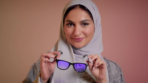 اتباع آخر صيحات الموضة, تصوير مقرب لإمرأة عربية خليجية سعودية مبتسمة ترتدي الحجاب والعباءة تقوم بوضع النظارة، الأناقة والاهتمام بالمظهر الخارجي، سيدة اماراتية تقوم بالعروض الإعلانية التسويقية للمنتجات المحلية، عرض احدث موديلات النظارات الشمسية، خلفية ملونة
