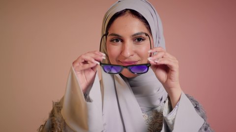 العروض الإعلانية التسويقية للمنتجات المحلية، الأناقة والاهتمام بالمظهر الخارجي، سيدة اماراتية تقوم بعرض احدث موديلات النظارات الشمسية، اتباع آخر صيحات الموضة, تصوير مقرب لإمرأة عربية خليجية سعودية مبتسمة ترتدي الحجاب والعباءة تقوم بوضع النظارة، خلفية ملونة