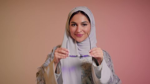 العروض الإعلانية التسويقية للمنتجات المحلية، الأناقة والاهتمام بالمظهر الخارجي، سيدة اماراتية تقوم بعرض احدث موديلات النظارات الشمسية، اتباع آخر صيحات الموضة, تصوير مقرب لإمرأة عربية خليجية سعودية مبتسمة ترتدي الحجاب والعباءة تقوم بوضع النظارة، خلفية ملونة