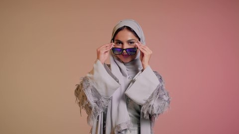 ارتداء النظارة والاهتمام بالمظهر الخارجي والاناقة الشخصية، سيدة اماراتية تقوم بعرض احدث موديلات النظارات الشمسية، متابعة آخر صيحات الموضة, تصوير مقرب لإمرأة عربية خليجية سعودية مبتسمة ترتدي الحجاب والعباءة تقوم بالتسويق للمنتجات المحلية، خلفية ملونة