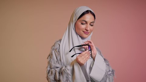 ارتداء النظارة والاهتمام بالمظهر الخارجي والاناقة الشخصية، سيدة اماراتية تقوم بعرض احدث موديلات النظارات الشمسية، متابعة آخر صيحات الموضة, تصوير مقرب لإمرأة عربية خليجية سعودية مبتسمة ترتدي الحجاب والعباءة تقوم بالتسويق للمنتجات المحلية، خلفية ملونة