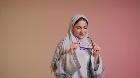العروض الإعلانية التسويقية للمنتجات المحلية، الأناقة والاهتمام بالمظهر الخارجي، سيدة اماراتية تقوم بعرض احدث موديلات النظارات الشمسية، اتباع آخر صيحات الموضة, تصوير مقرب لإمرأة عربية خليجية سعودية مبتسمة ترتدي الحجاب والعباءة تقوم بوضع النظارة، خلفية ملونة