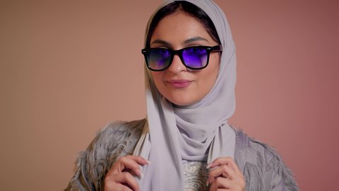 العروض الإعلانية التسويقية للمنتجات المحلية، الأناقة والاهتمام بالمظهر الخارجي، سيدة اماراتية تقوم بعرض احدث موديلات النظارات الشمسية، اتباع آخر صيحات الموضة, تصوير مقرب لإمرأة عربية خليجية سعودية مبتسمة ترتدي الحجاب والعباءة تقوم بوضع النظارة، خلفية ملونة