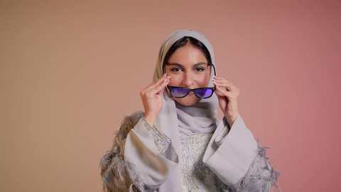 عرض احدث موديلات النظارات الشمسية، متابعة آخر صيحات الموضة, تصوير مقرب لإمرأة عربية خليجية سعودية مبتسمة ترتدي الحجاب والعباءة تقوم بوضع النظارة، الأناقة والاهتمام بالمظهر الخارجي، سيدة اماراتية تقوم بالعروض الإعلانية التسويقية للمنتجات المحلية، خلفية ملونة