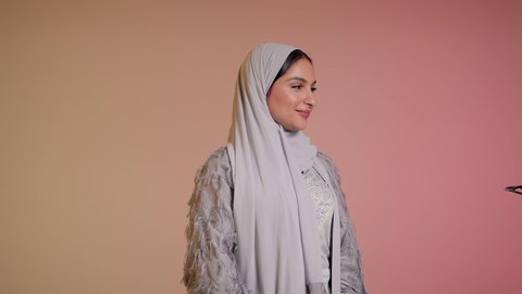 التسويق للمنتجات المحلية، الأناقة والاهتمام بالمظهر الخارجي، سيدة اماراتية تقوم بعرض احدث موديلات النظارات الشمسية، اتباع آخر صيحات الموضة, تصوير مقرب لإمرأة عربية خليجية سعودية مبتسمة ترتدي الحجاب والعباءة تقوم بوضع النظارة، خلفية ملونة