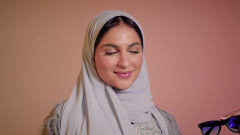 تعابير الدهشة والسرور، ارتداء النظارة والاهتمام بالمظهر الخارجي والاناقة الشخصية، سيدة اماراتية تقوم بعرض احدث موديلات النظارات الشمسية، تصوير مقرب لإمرأة عربية خليجية سعودية مبتسمة ترتدي الحجاب والعباءة تقوم بالتسويق للمنتجات المحلية، خلفية ملونة