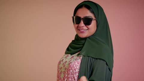 الشراء من الاسواق والمتاجر،  الاُثر الايجابي للتسوق، شابة اماراتية تمسك الحقائب بإيماءات السرور، الاستفادة من العروض والتخفيض الموسمي، تصوير مقرب لامرأة عربية خليجية سعودية ترتدي العباءة والحجاب تحمل بيديها الاكياس، اقتناء الهدايا والمستلزمات، خلفية ملونة