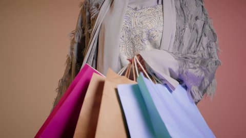 اقتناء الهدايا والمستلزمات، الشراء من الاسواق والمتاجر، سيدة اماراتية تمسك الحقائب بإيماءات السرور، الاُثر الايجابي للتسوق، الاستفادة من العروض والتخفيض الموسمي، تصوير مقرب لامرأة عربية خليجية سعودية ترتدي العباءة والحجاب تحمل بيديها الاكياس، خلفية ملونة