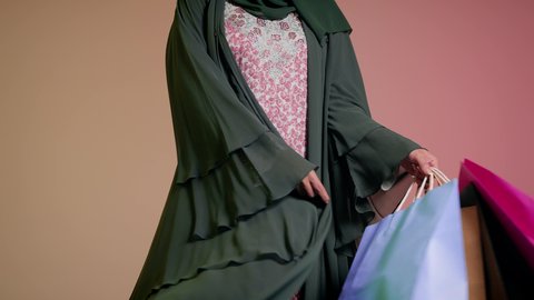 الاستفادة من العروض والتخفيض الموسمي، شراء الهدايا والمستلزمات، الاُثر الايجابي للتسوق على نفسية النساء، تصوير مقرب لامرأة عربية خليجية سعودية ترتدي العباءة والحجاب تحمل بيديها أكياس ملونة، سيدة اماراتية تمسك الحقائب بإيماءات السرور، خلفية ملونة