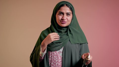 عطورات عربية خليجية، التسويق للعطور والزيوت الطبيعية الخليجية و العالمية، سيدة اماراتية تسوق للمنتجات العطرية، تصوير مقرب لإمرأه عربيه سعودية محجبة ترتدي العباءة تقوم برش العطر، التطيب والتعطر بالعود العطري، خلفية ملونة