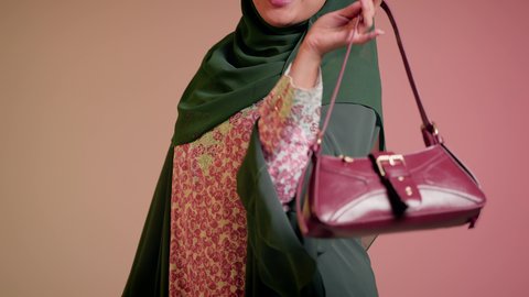 الاهتمام بالمظهر الخارجي والاناقة، متابعة آخر صيحات الموضة, شراء بضائع الماركات العالمية، تصوير مقرب لامرأة عربية خليجية اماراتية ترتدي الحجاب والعباءة مع النظارات الشمسية تقف باستقامة بتعابير الثقة بالنفس، سيدة سعودية تنظر الى الكاميرا وتحمل بيدها حقيبة حمراء، خلفية ملونة